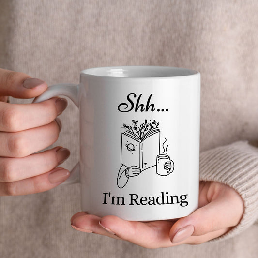 White ceramic 11oz coffee mug with 'Shh... I'm Reading' design held by a girl. Bookworm coffee cup, book lover gift.