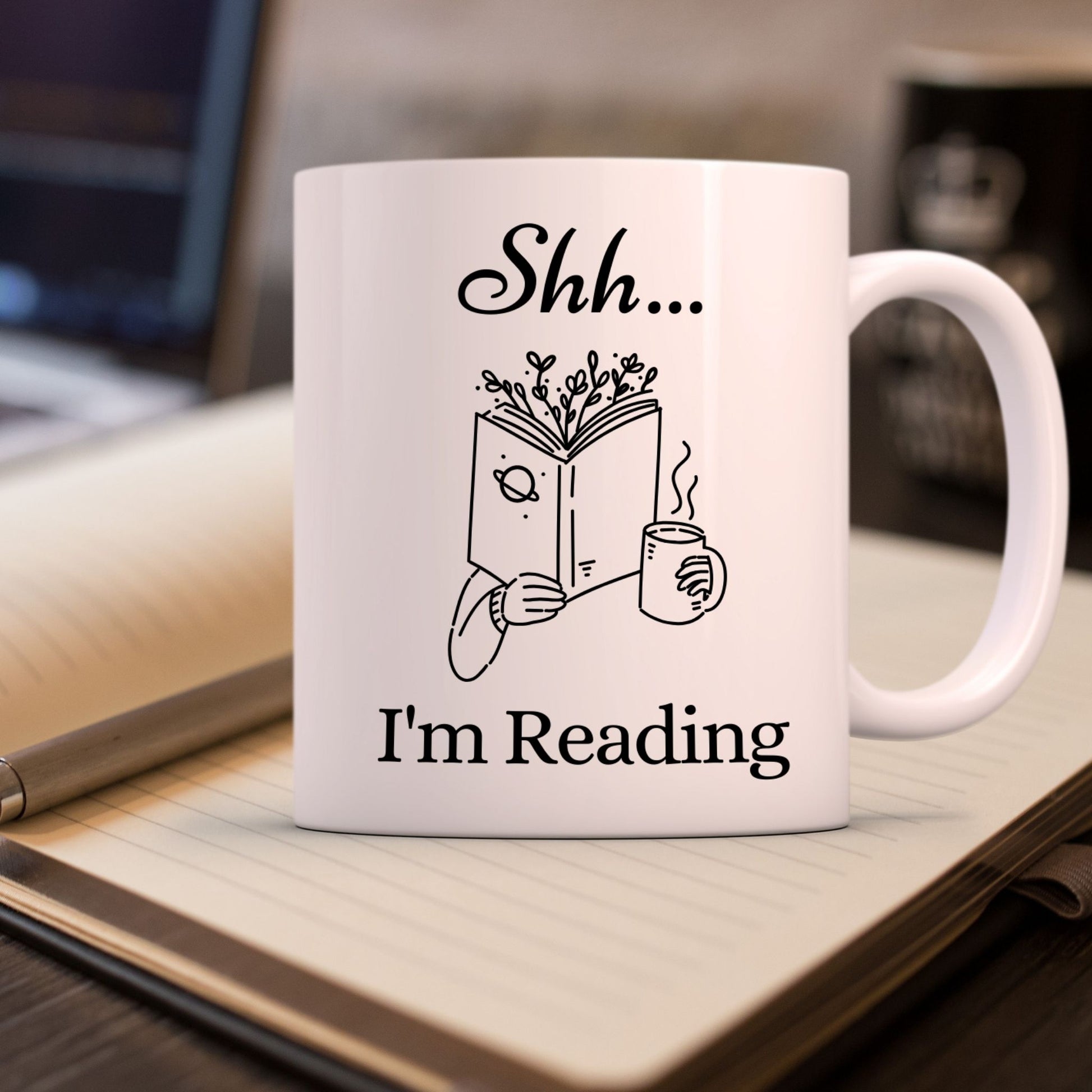 "Shh... I’m Reading" mug placed on a notebook. Funny bookish mug for bibliophiles.