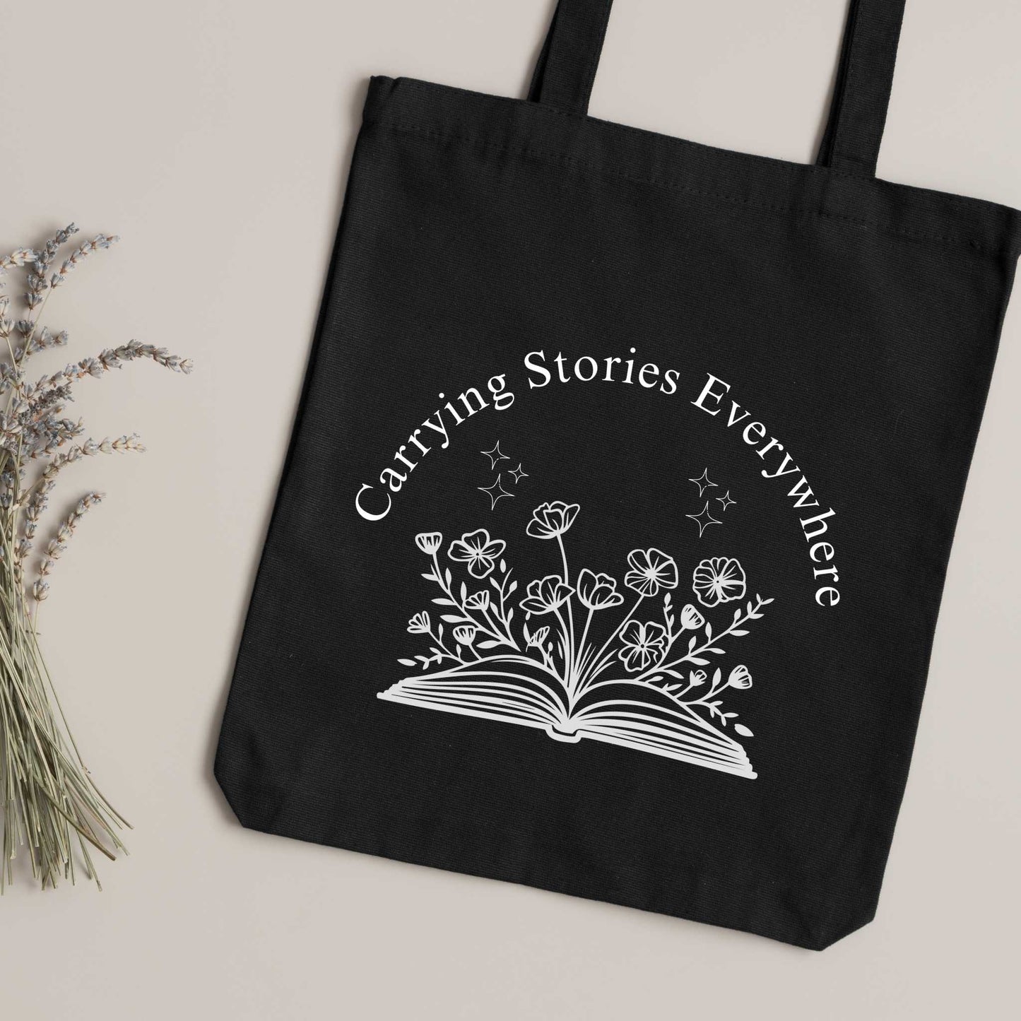 Black book lover tote bag with 'Carrying Stories Everywhere' text & floral book illustration – aesthetic bookish shoulder bag for everyday use.