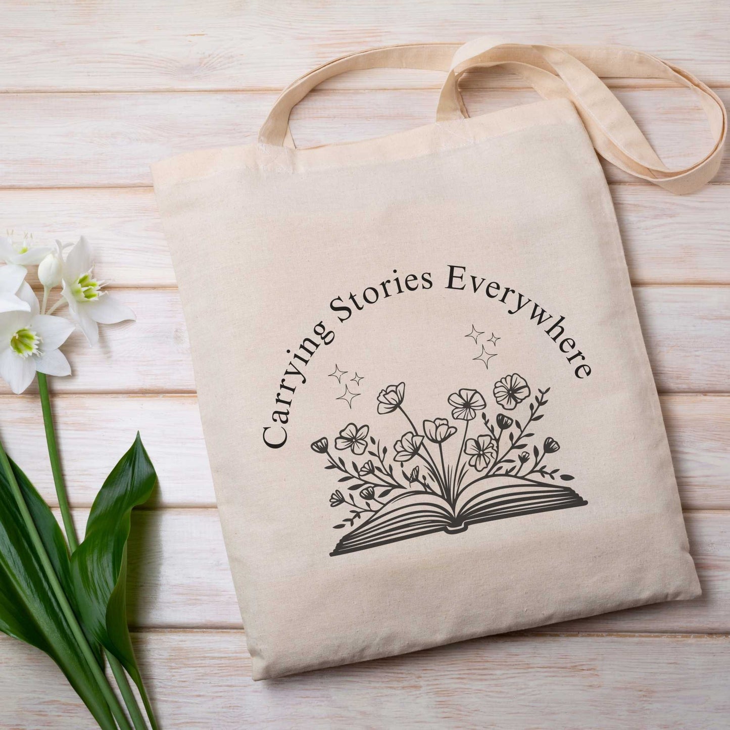 Bookish natural tote bag with text 'Carrying Stories Everywhere' & floral book design – reusable canvas library tote for bibliophiles and students